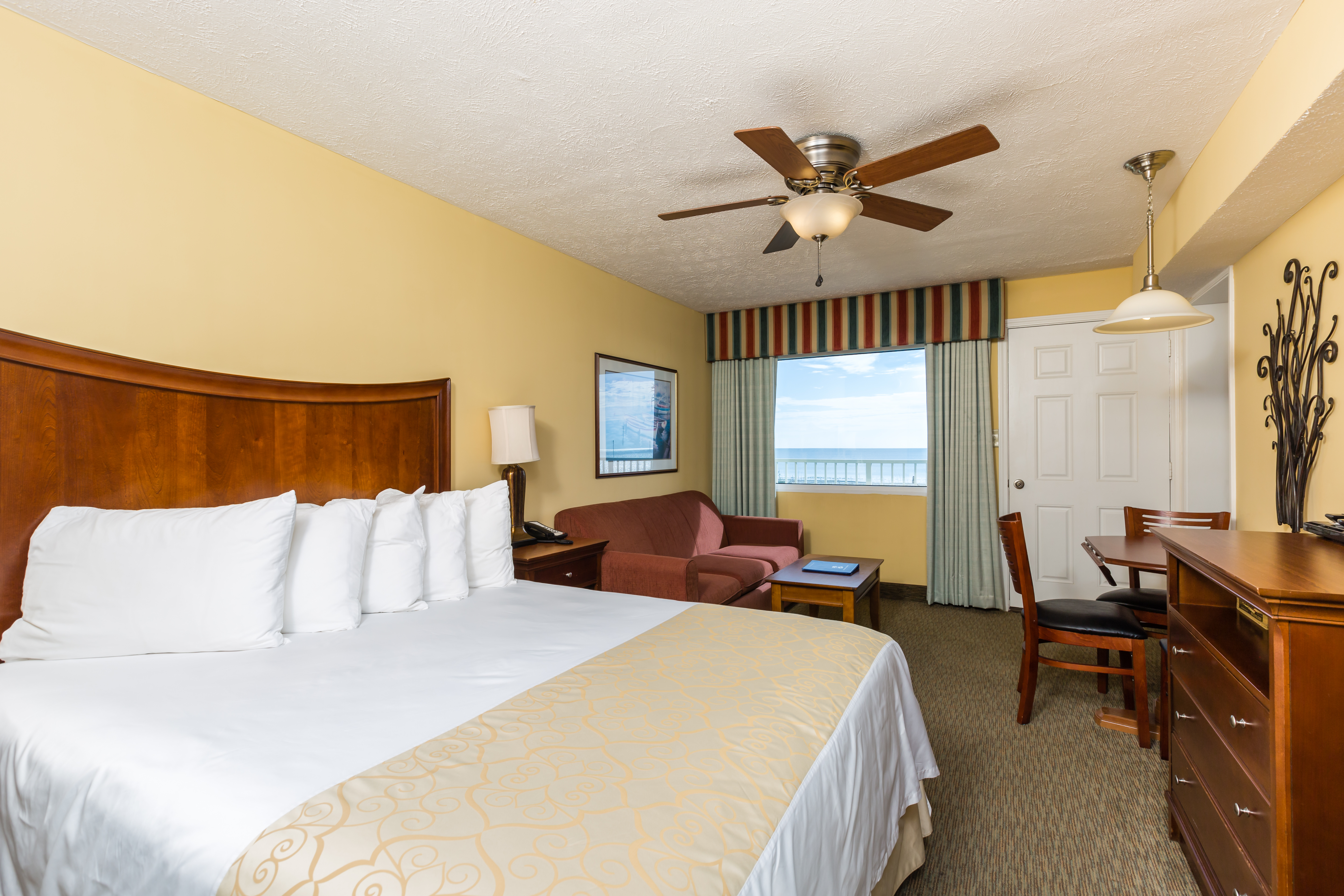 A hotel room with a large bed, desk, chair, and window with an ocean view.