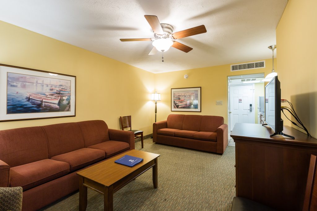 A hotel living room with two red couches, a wooden coffee table, a TV on a stand, and a doorway in the background.